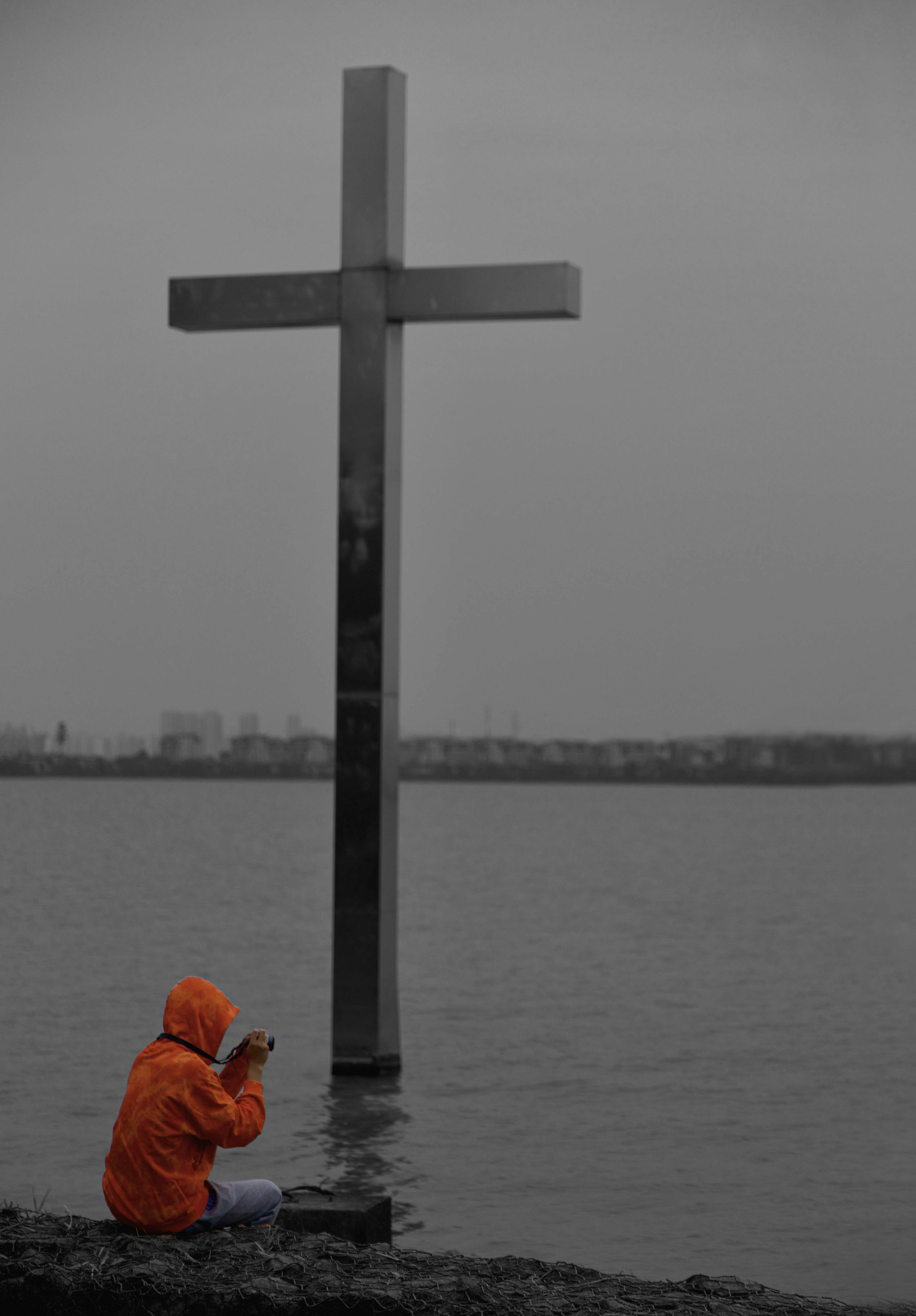 a person sitting on a rock next to a large cross