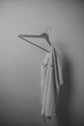 Minimalist beige blouse hanging on a simple white hanger against a clean white wall.