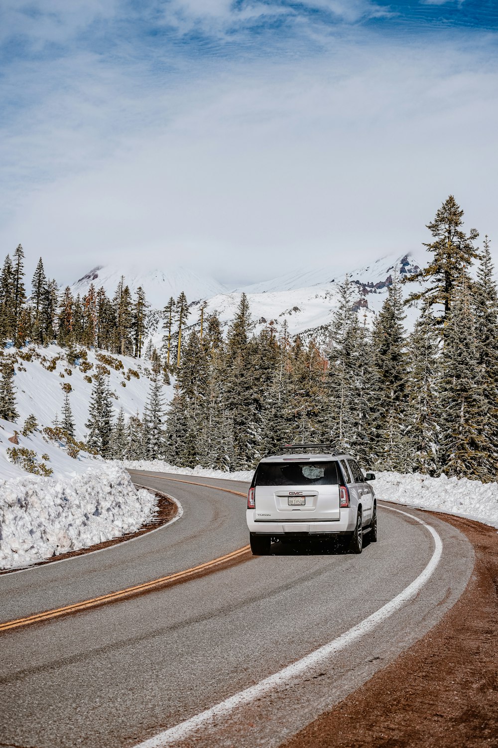 a white car driving on a road with snow on the side