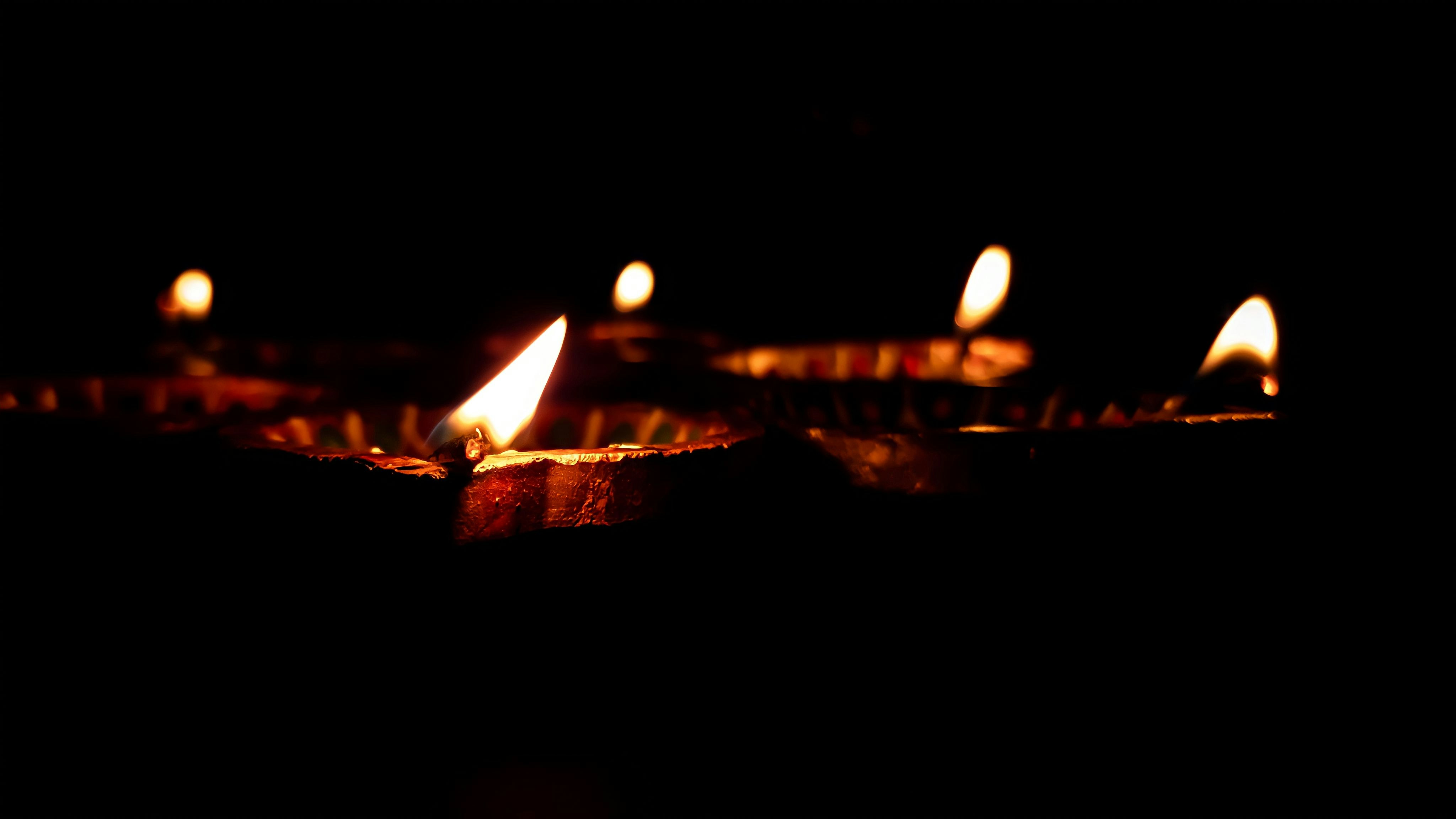 Hands carefully lighting small clay diyas at a river ghat at dawn with soft warm light