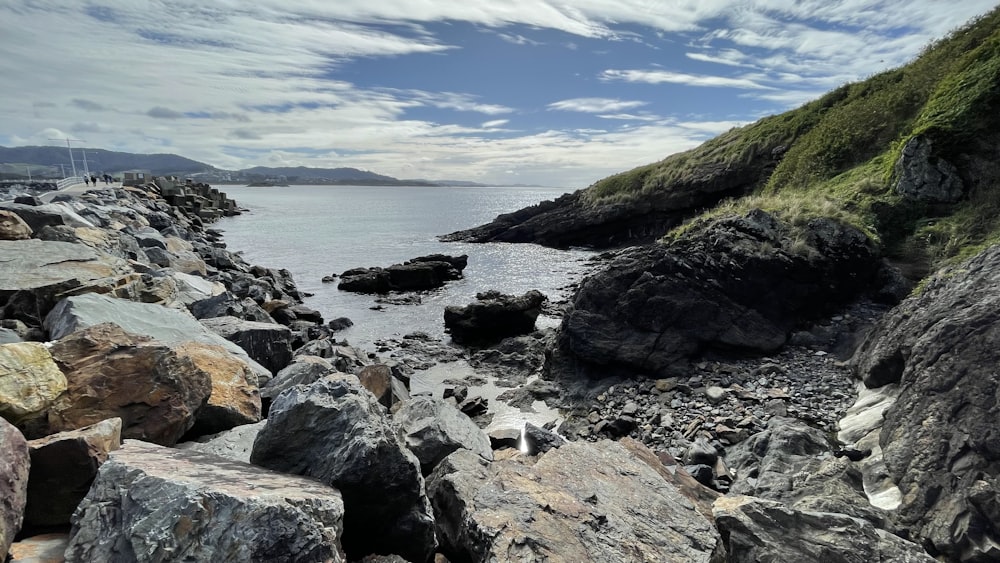 a rocky beach with a hill and water in the background