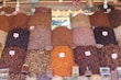 A vibrant market stall displays a variety of dried fruits, nuts, and spices organized in neat piles. Each pile is labeled with a price tag in the local currency. The arrangement creates a visually appealing pattern with various textures and colors.