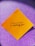A yellow square paper with a motivational quote written in black script font is placed against a sparkly purple background.