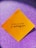 A yellow square paper with a motivational quote written in black script font is placed against a sparkly purple background.