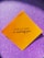 A yellow square paper with a motivational quote written in black script font is placed against a sparkly purple background.