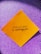 A yellow square paper with a motivational quote written in black script font is placed against a sparkly purple background.