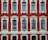 A facade of a historic building featuring six large, arched windows with intricate white stucco detailing set against a deep red background. The windows are symmetrically arranged in two rows with decorative elements above and below each window. The architectural style suggests elegance and classical influences.
