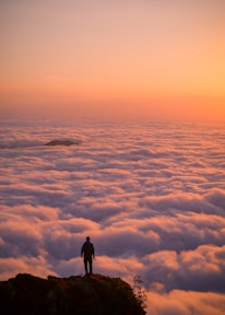 A traveler standing on a cliff overlooking a vast tropical landscape at sunset.