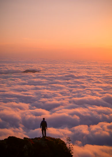 A vibrant photo of a traveler standing on a cliff overlooking a colorful sunset over the ocean.