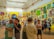A vibrant art gallery room with high ceilings, ornate moldings, and brightly colored walls displaying an eclectic mix of artwork. People are engaged in discussions, and some are examining the artworks closely. The atmosphere suggests active interest and engagement with the art pieces.