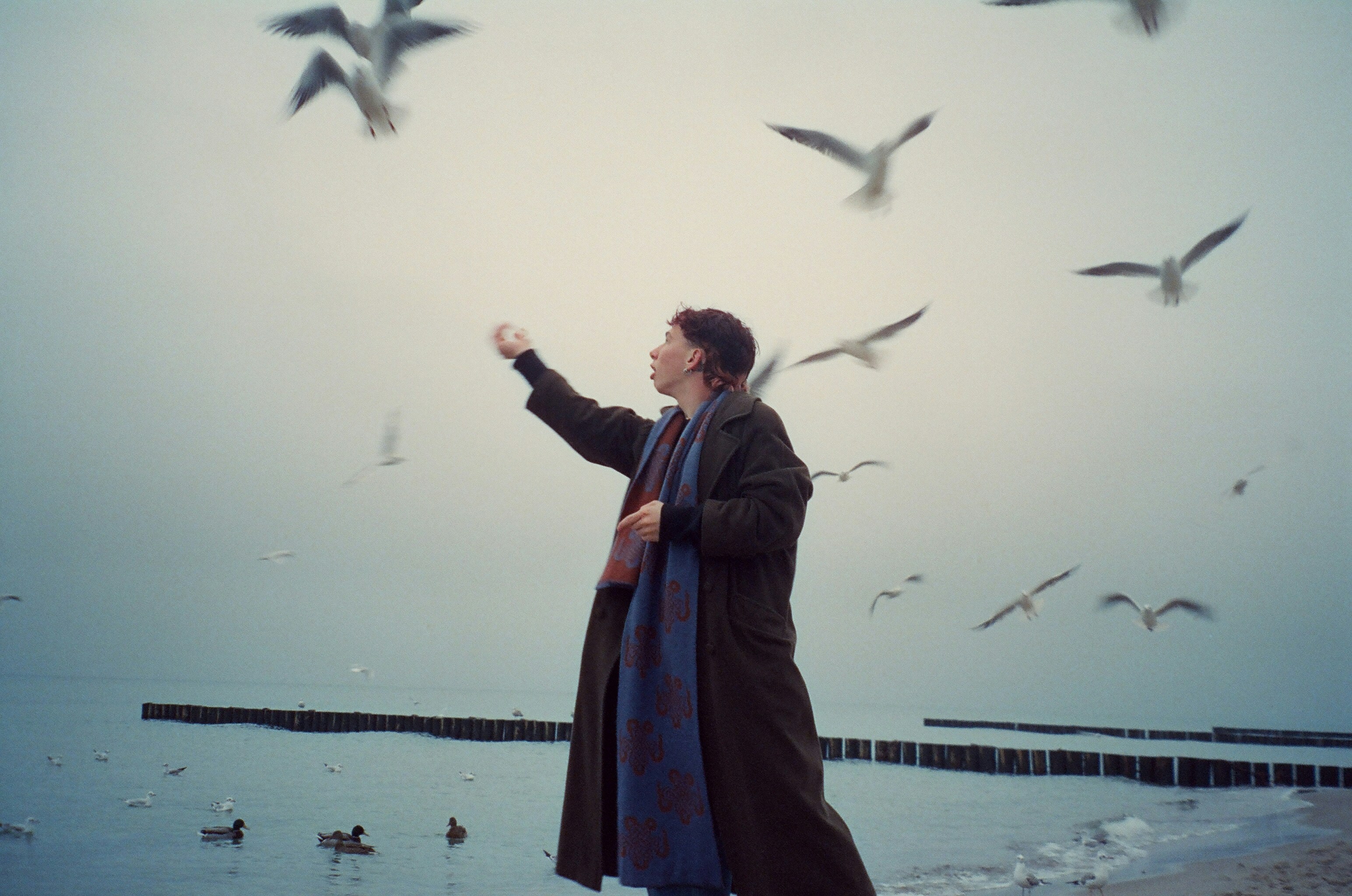 a person in a robe standing in front of a body of water with birds flying around