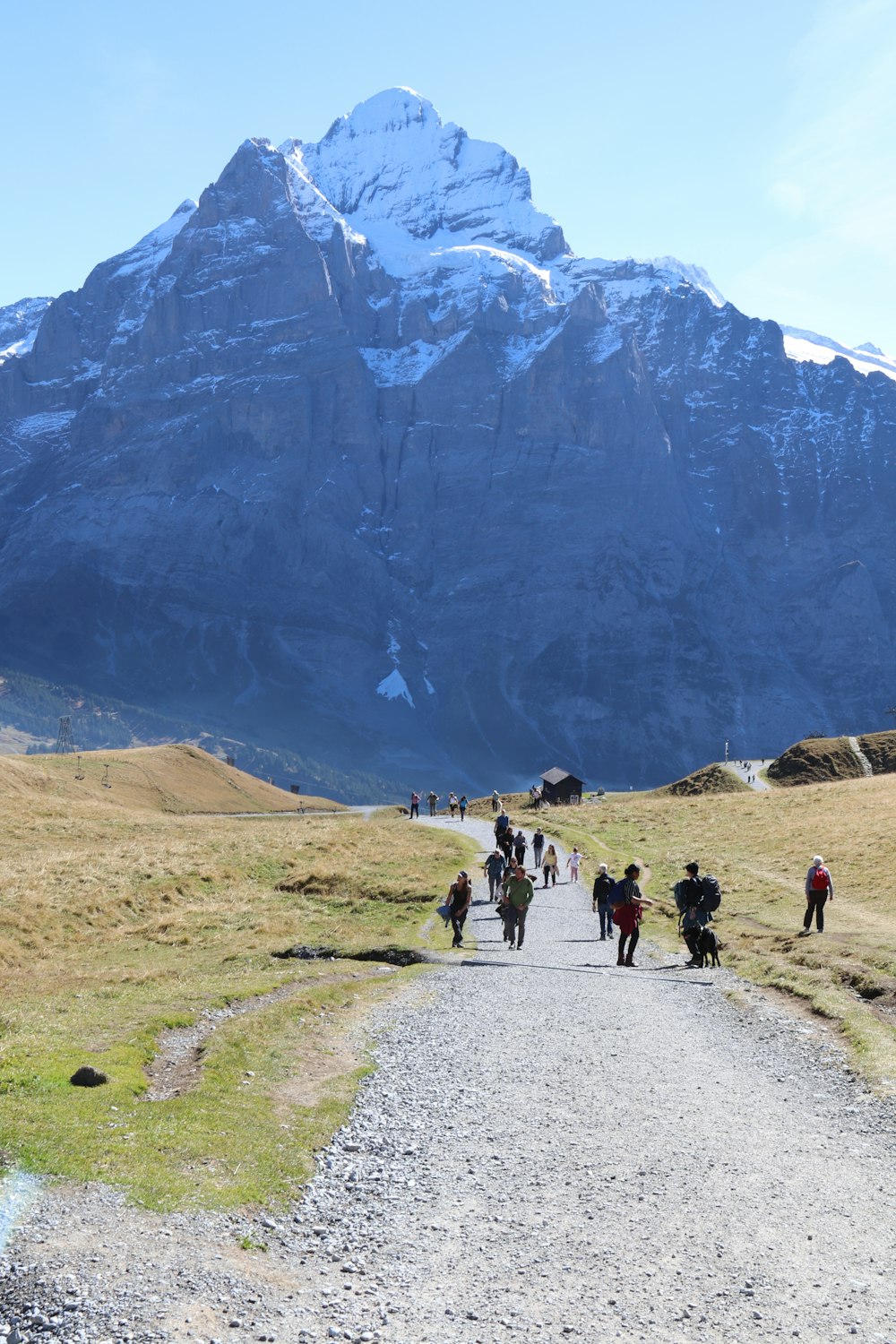 a group of people walking on a dirt road in front of a large mountain