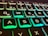 Close-up view of an illuminated computer keyboard featuring keys highlighted with a green and blue backlight. The focus is mainly on the QWERTY layout, with keys such as Q, W, E, A, S, and D clearly visible.