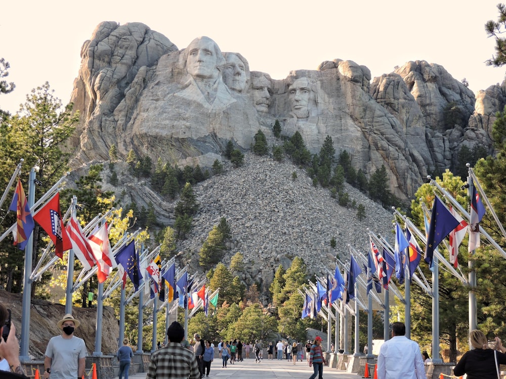 un grupo de personas caminando por un sendero con banderas y el Monumento Nacional del Monte Rushmore al fondo