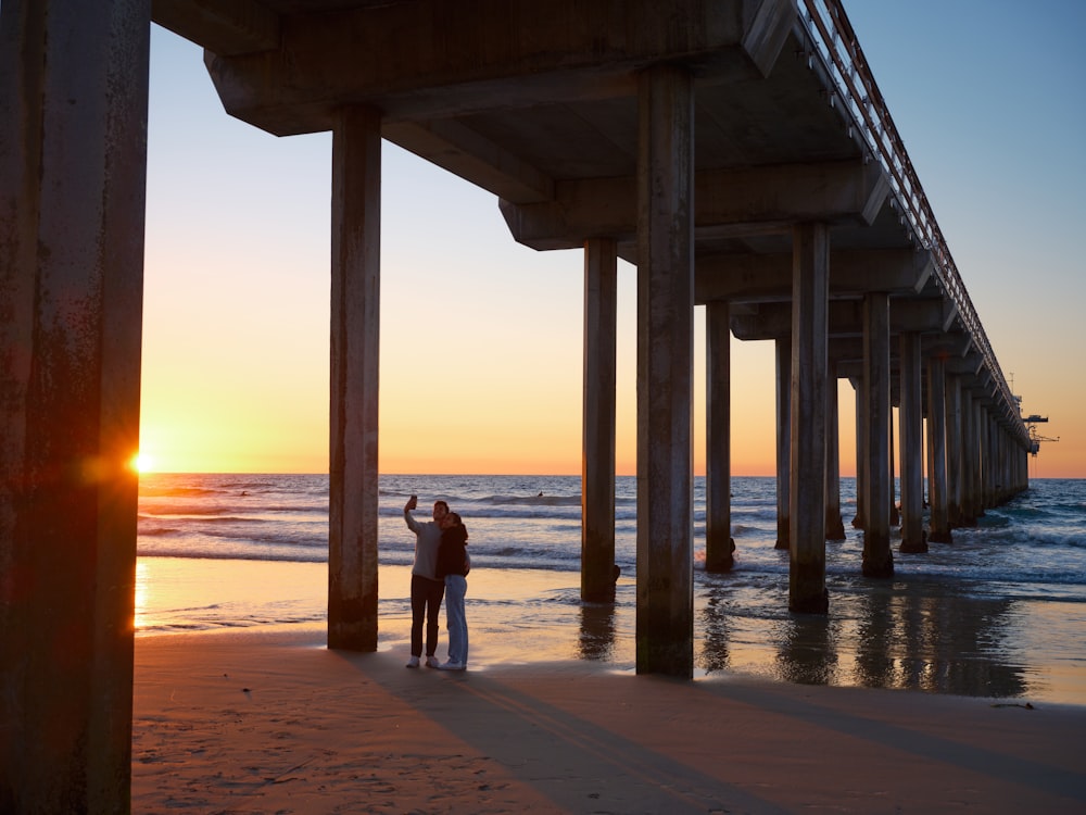 a couple standing under a wooden structure on a beach