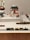 A display of vintage toys including a colorful wooden train set on tracks, multiple model airplanes, a toy ship, and other small toy vehicles arranged in a diorama-like setting. The background features signage and architectural elements that resemble a transportation or airport theme.
