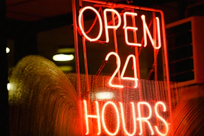 Nighttime exterior shot of Posto Amizade, showing the 24-hour open sign lit up.