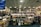 A spacious bookstore with multiple shelves filled with books, including a sale section in the center. The store features a modern design with a high ceiling and circular light fixtures. Several people are browsing the books, and signs such as 'PLEASE PAY HERE' and 'CUSTOMER SERVICES' are visible.