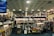 A spacious bookstore with multiple shelves filled with books, including a sale section in the center. The store features a modern design with a high ceiling and circular light fixtures. Several people are browsing the books, and signs such as 'PLEASE PAY HERE' and 'CUSTOMER SERVICES' are visible.