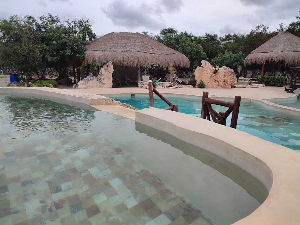 a pool with a chair and a hut in the background