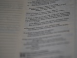 The image displays a close-up of a book page with text in a column, presenting portions of a passage. Part of the text is highlighted with a darker shade to differentiate certain sections.