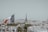 A panoramic view of a cityscape with the Eiffel Tower prominently in the background. In the foreground, a French flag is visible, flying atop a building. The landscape is densely packed with classic architecture and rooftops, with hints of greenery scattered throughout.