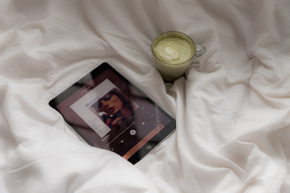 a cell phone and a cup of tea on a bed