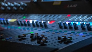An artistic photo of sound mixing equipment with colorful LED indicators glowing.