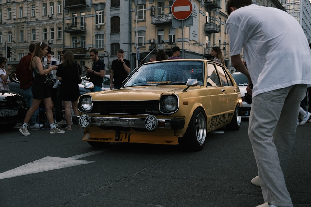 a man standing next to a yellow car on a street with people