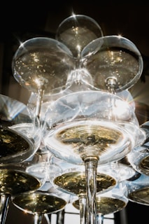 Champagne glasses stacked in a pyramid formation create a sparkling and elegant display. The light reflecting off the glasses enhances their transparency, showcasing the liquid's amber hue. The overall composition conveys a sense of celebration and sophistication.