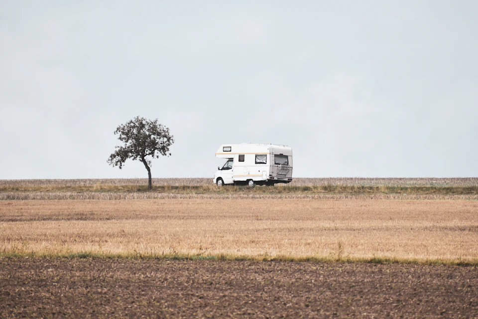 White camper van parked on dirt road surrounded by tall grasses and open field
