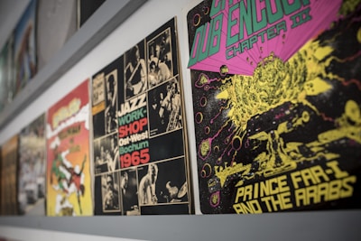 A collection of vibrant vintage album covers is displayed along a wall. The album on the right features psychedelic artwork with a cosmic theme, using bright green, pink, and yellow colors. Next to it, a monochrome jazz-themed cover from 1965 is visible, featuring black and white photos of musicians and bold text.