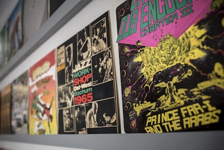 A collection of vibrant vintage album covers is displayed along a wall. The album on the right features psychedelic artwork with a cosmic theme, using bright green, pink, and yellow colors. Next to it, a monochrome jazz-themed cover from 1965 is visible, featuring black and white photos of musicians and bold text.