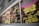 A collection of vibrant vintage album covers is displayed along a wall. The album on the right features psychedelic artwork with a cosmic theme, using bright green, pink, and yellow colors. Next to it, a monochrome jazz-themed cover from 1965 is visible, featuring black and white photos of musicians and bold text.
