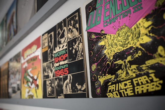 A collection of vibrant vintage album covers is displayed along a wall. The album on the right features psychedelic artwork with a cosmic theme, using bright green, pink, and yellow colors. Next to it, a monochrome jazz-themed cover from 1965 is visible, featuring black and white photos of musicians and bold text.