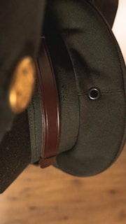 Close-up view of a dark green military-style hat with a brown leather strap and a metallic eyelet.