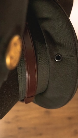 Close-up view of a dark green military-style hat with a brown leather strap and a metallic eyelet.