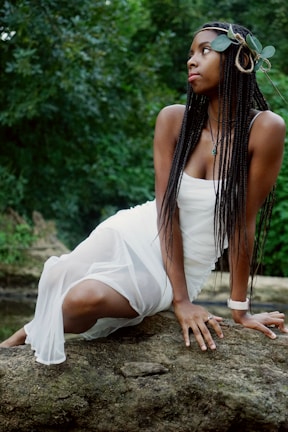 A woman wearing a unique artisan bracelet while sitting on a rock in a lush forest.