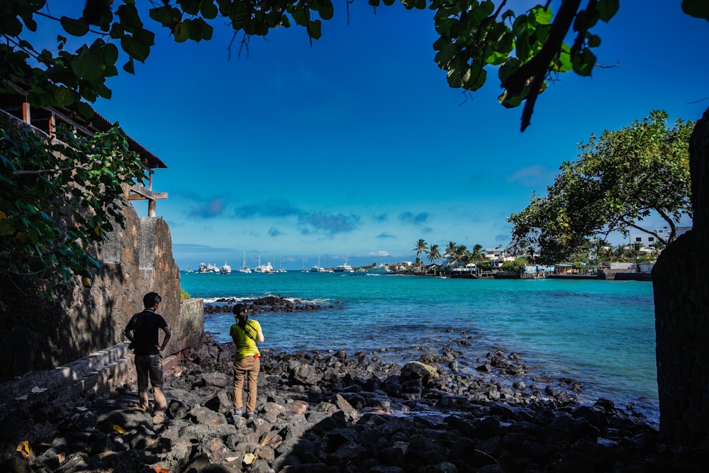 Un couple de personnes debout sur une plage rocheuse regardant l’océan