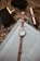 A rose gold wristwatch is neatly placed on top of an open magazine with visible text. Nearby, there's a black and gold perfume bottle and a gold lipstick tube on a patterned wooden surface.