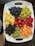 A platter filled with a variety of fresh fruits including blueberries, green grapes, raspberries, strawberries, pineapple chunks, blackberries, kiwi slices, and cantaloupe cubes, all arranged neatly on a white tray with handles.