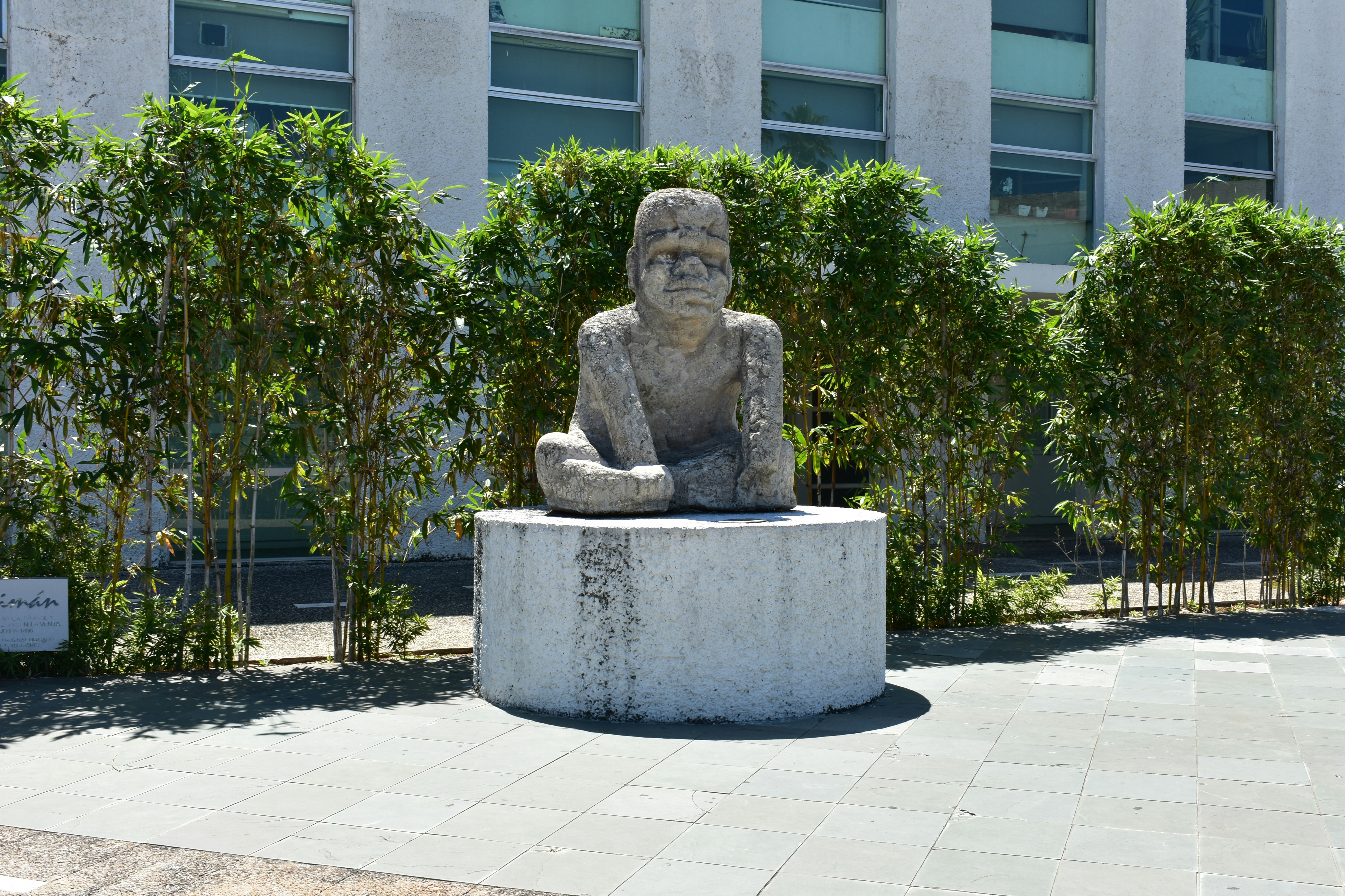 a statue of a person sitting on a stone bench in front of a building