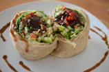 A colorful wrap filled with fresh veggies and melted cheese, sliced diagonally.