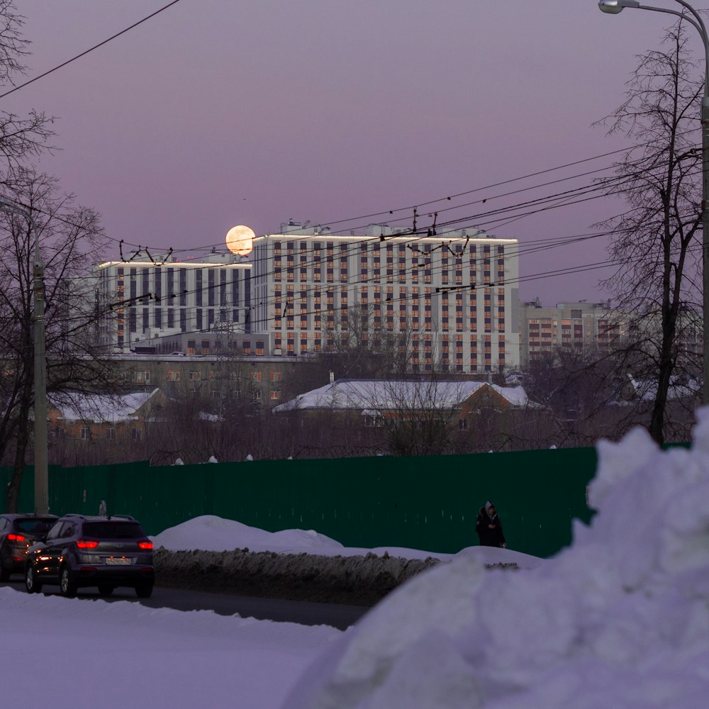 a building with a green fence and a street with cars and snow