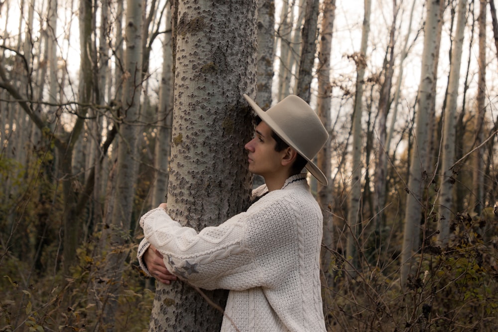 a person in a hat leaning against a tree