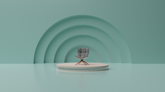 A modern, minimalist setting with a single gray chair positioned on a circular platform. The background features three large, semi-circular ridges creating an arch-like pattern. The overall color scheme is a calm, muted teal.