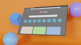 A digital illustration features a web browser interface with the Firefox logo prominently displayed. The browser window is set against a vibrant orange background and surrounded by colorful geometric shapes including a blue cube, a light blue sphere, and a purple sphere. The browser window shows a search bar and several rectangular buttons below it.