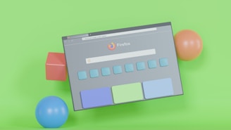 A tilted browser window, featuring the Firefox logo and search bar, is displayed against a vibrant green background. Surrounding the window are colorful 3D geometric shapes, including a red cube, a blue sphere, and an orange sphere.