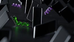 A surreal scene featuring a green, worm-like object with a glossy, translucent appearance. It is set among numerous floating, black rectangular shapes resembling smartphones. In the background, two abstract, purple spiral forms add to the sense of surrealism and abstraction.