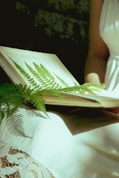 ein aufgeschlagenes Buch im Schoße einer Person, ein Farnblatt dabei